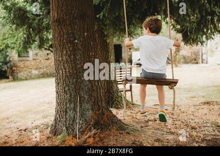 Vue arrière du garçon sur balançoire sous les arbres Banque D'Images