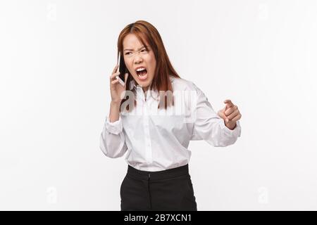 Une jeune femme asiatique en colère et tentée, agressive, qui se courbe au téléphone, est indignée par la colère et l'irritation, criant en dynamique mobile Banque D'Images