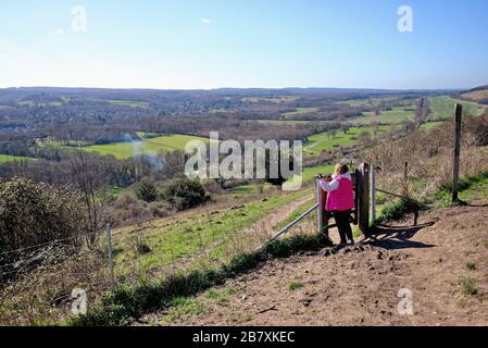 Une femme promenant dans un manteau rouge en regardant la vue de Ranmore Common sur les North Downs le jour ensoleillé du printemps, près de Dorking Surrey Angleterre Royaume-Uni Banque D'Images