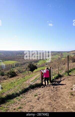 Une femme promenant dans un manteau rouge en regardant la vue de Ranmore Common sur les North Downs le jour ensoleillé du printemps, près de Dorking Surrey Angleterre Royaume-Uni Banque D'Images