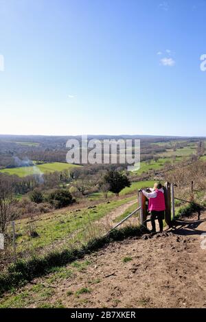 Une femme promenant dans un manteau rouge en regardant la vue de Ranmore Common sur les North Downs le jour ensoleillé du printemps, près de Dorking Surrey Angleterre Royaume-Uni Banque D'Images