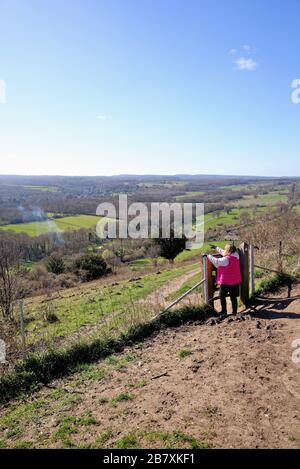 Une femme promenant dans un manteau rouge en regardant la vue de Ranmore Common sur les North Downs le jour ensoleillé du printemps, près de Dorking Surrey Angleterre Royaume-Uni Banque D'Images