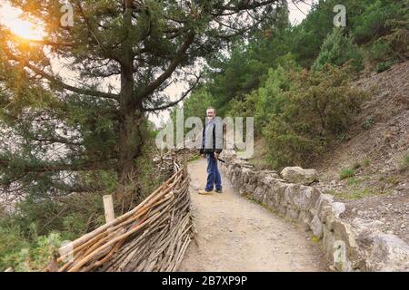 Un homme âgé dans une veste debout sur le sentier Golitsyn dans le village de Novy Svet, Crimée et souriant à la caméra. Soirée dans le village de villégiature Banque D'Images