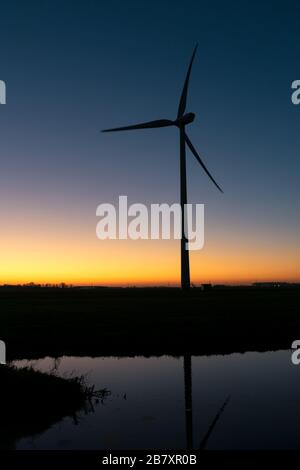 Silhouette d'une grande éolienne contre un ciel coloré en soirée Banque D'Images