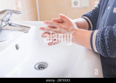 Gros plan des mains savonnelles d'un enfant lavées sous l'eau courante dans un évier Banque D'Images