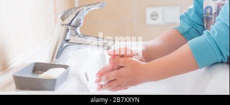 Gros plan des mains savonnelles d'un enfant lavées sous l'eau courante dans un évier Banque D'Images