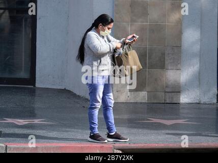 Los Angeles, Californie, États-Unis. 18 mars 2020. Une femme portant un masque se tient sur Hollywood Boulevard le mercredi 18 mars 2020, à Los Angeles, en Californie. Le gouverneur californien Gavin Newsom Sunday a appelé tous les bars californiens à fermer et à tous les aînés à s'isoler. De nombreux cinémas et autres lieux publics ont fermé leurs portes, tandis que d'autres entreprises restent ouvertes pour des affaires normales, comme la propagation de Coronavirus (COVID-19) continue. Crédit: Ringo Chiu/ZUMA Wire/Alay Live News Banque D'Images