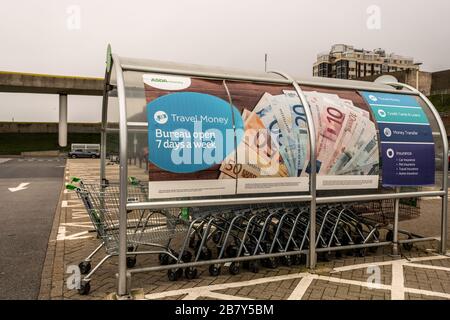 Publicité pour le change de devises sur un point de collecte de trolleybus dans un parking vide de supermarché pendant la pandémie de Coronavirus, East Sussex, Royaume-Uni. Banque D'Images