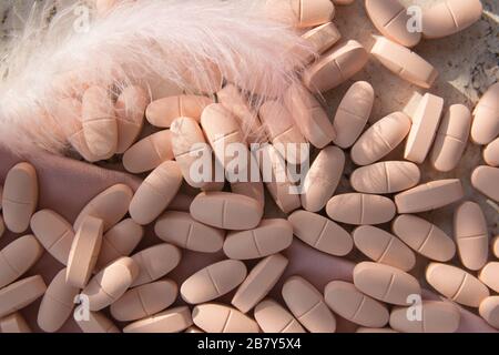 Pilules ou vitamines sur le fond de bois naturel avec tissu de soie rose et plume en été. Vue de dessus. Banque D'Images