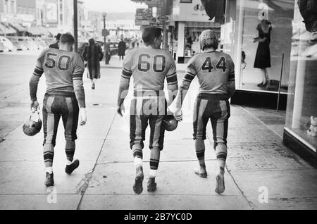 Vue arrière de trois joueurs de football de High School dans Uniforms marchant sur Street, Minot, Dakota du Nord, États-Unis, John Vachon pour l'Administration américaine de la sécurité agricole, octobre 1940 Banque D'Images