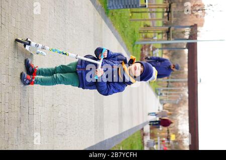 POZNAN, POLOGNE - 08 mars 2020: Jeune garçon portant des vêtements chauds avec un scooter debout sur un sentier du parc Rataje. Banque D'Images