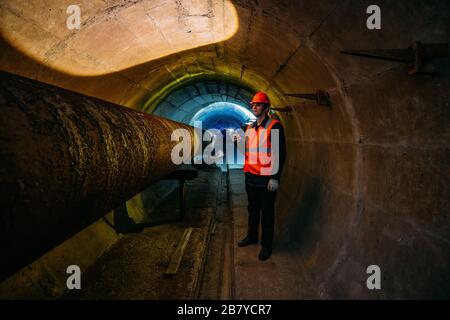 Le travailleur du tunnel examine le pipeline dans le tunnel souterrain Banque D'Images