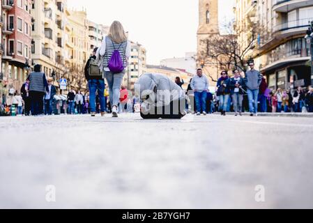 Valence, Espagne - 8 mars 2020: Le jeune mendiant s'agenouillant et se croise dans une rue animée mendiant pour des almes. Banque D'Images