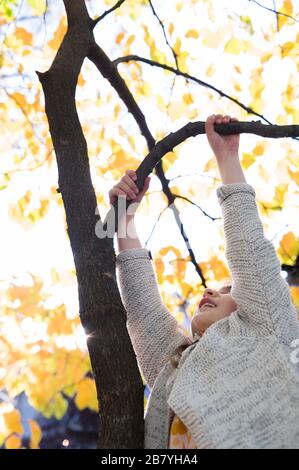 Fille grimpant arbre pendant l'automne Banque D'Images