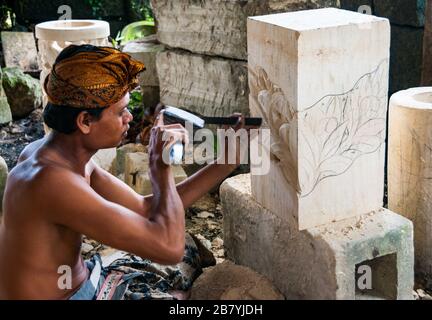 Un artisan balinais à l'œuvre de la sculpture d'une statue d'un bloc de pierre Banque D'Images