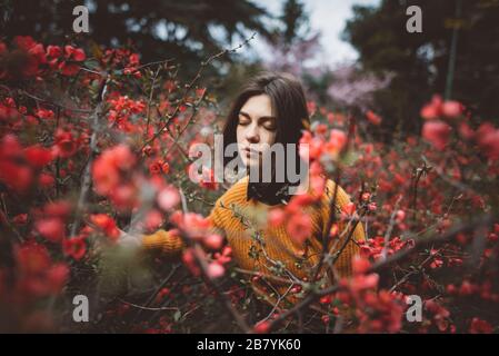 Jeune femme avec les yeux fermés dans des arbustes avec des fleurs rouges Banque D'Images