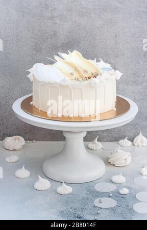 Élégant gâteau blanc décoré de chocolat blanc fondu, de meringues, de papier gaufré et de macarons. Banque D'Images