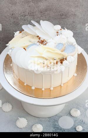 Élégant gâteau blanc décoré de chocolat blanc fondu, de meringues, de papier gaufré et de macarons. Banque D'Images