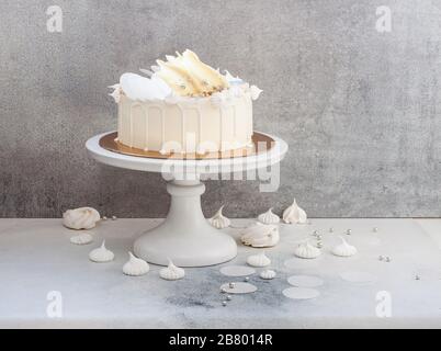 Élégant gâteau blanc décoré de chocolat blanc fondu, de meringues, de papier gaufré et de macarons. Banque D'Images