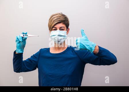 Femme confinée mesurant sa température corporelle avec un thermomètre pour le coronavirus covid-19 regardant et gestant avec son pouce montrant que tout Banque D'Images