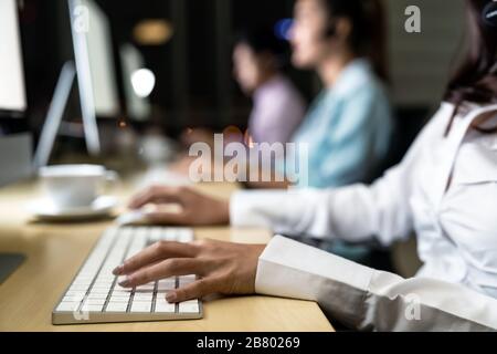 Gros plan l'équipe de collègues de l'opérateur de confiance des jeunes adultes asiatiques avec des micro-casques travaillant dans un centre d'appels la nuit en tant que service à la clientèle et support technique Banque D'Images