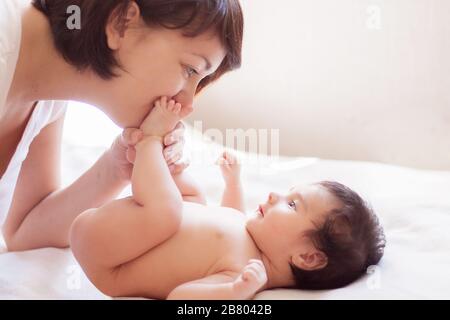 Belle maman et bébé se trouvent sur le plat blanc. Maman embrasse les talons du bébé. Espace de copie Banque D'Images