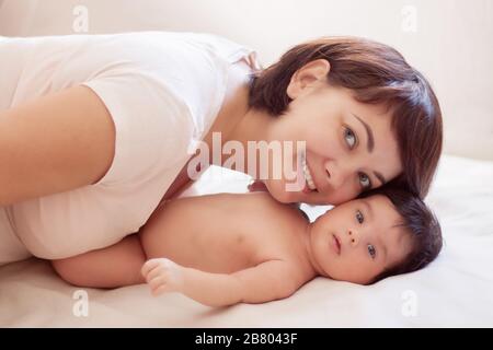 Belle maman et bébé se trouvent sur le plat blanc, souriant et vue à l'appareil photo Banque D'Images