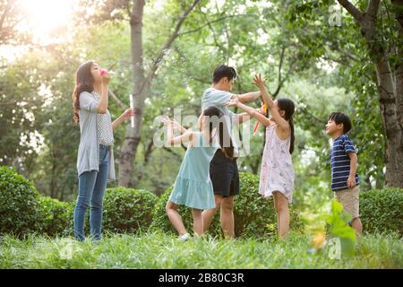 Une jeune famille chinoise heureuse soufflait de bulles sur l'herbe Banque D'Images