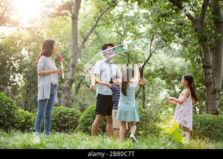 Une jeune famille chinoise heureuse soufflait de bulles sur l'herbe Banque D'Images