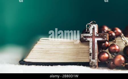 Gros plan sur la Sainte Bible et perles crucifix sur une vieille table ronde. Magnifique arrière-plan de mur vert. Banque D'Images