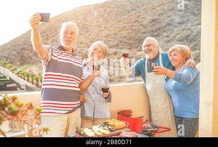 Joyeux amis seniors prenant un selfie avec un appareil photo de smartphone au barbecue dîner sur la terrasse de la maison - les personnes âgées s'amuser avec la nouvelle technologie de tendance Banque D'Images