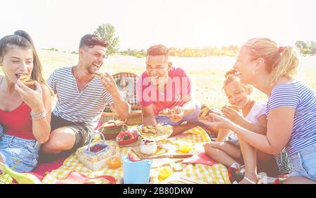 Les familles heureuses qui pique-niquent dans le parc naturel en plein air - les jeunes parents s'amusent avec les enfants en été, mangeant des gâteaux et riant ensemble - Love an Banque D'Images