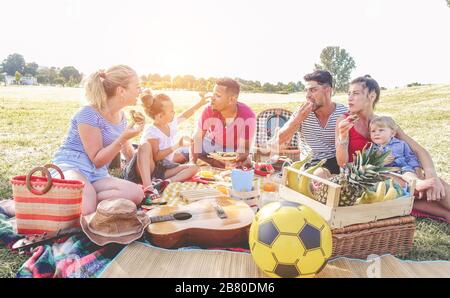 Les familles heureuses font un pique-nique dans le parc de la ville - les jeunes parents s'amusent avec leurs enfants en été, mangeant, riant et jouant ensemble - Love A. Banque D'Images