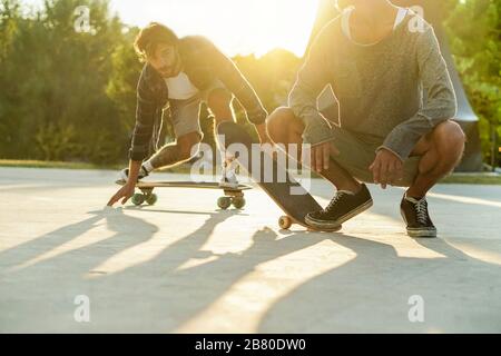 Les amis de Skater qui se produit avec des planches de surf dans le parc urbain avec rétro-éclairage- les jeunes qui s'amusent à faire du skateboard un sport extrême - se concentrer sur le rig Banque D'Images