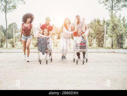 Jeunes millénaires les gens qui font de la course avec un panier - heureux amis fous s'amuser avec des chariots dans le parc de voiture du centre commercial - style de vie des jeunes et la fête Banque D'Images