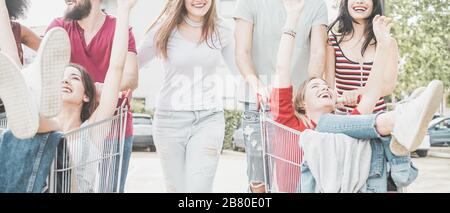 Jeunes millénaires les gens qui font de la course avec un panier - heureux amis fous s'amuser avec des chariots dans le parking - style de vie des jeunes et concept de fête - FO Banque D'Images