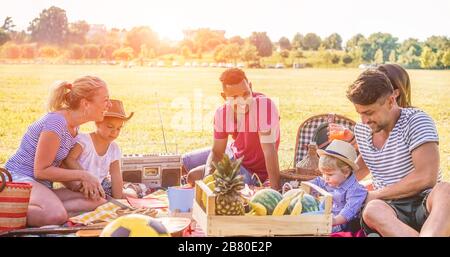 Les familles heureuses qui pique-niquent dans le parc naturel en plein air - les jeunes parents s'amusent avec les enfants en été en mangeant et en riant ensemble - moo positif Banque D'Images