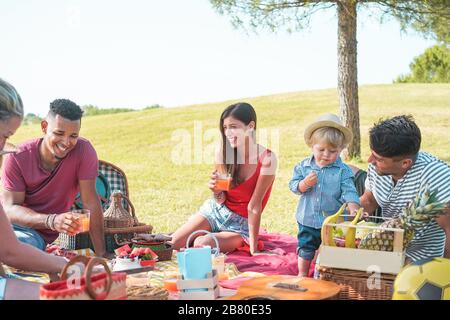 Les familles heureuses multiraciales pique-nique dans le parc extérieur - les jeunes parents s'amusent avec les enfants en été en mangeant ensemble - nourriture, le week-end le plus vivant Banque D'Images