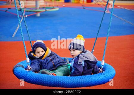 POZNAN, POLOGNE - 08 mars 2020: Deux jeunes garçons assis sur un équipement de balancement de filet dans une aire de jeux du parc Rataje. Banque D'Images