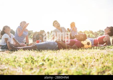 Les familles heureuses qui font un pique-nique dans le parc naturel - les jeunes parents s'amusent avec leurs enfants en été en mangeant, en buvant et en riant ensemble - l'amour Banque D'Images