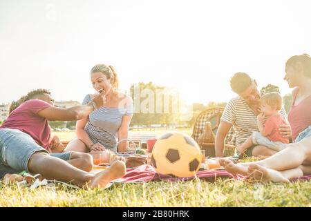 Familles heureuses multiraciales pique-nique dans le parc extérieur - jeunes parents s'amuser avec les enfants en été manger et jouer - nourriture, week-end frv Banque D'Images