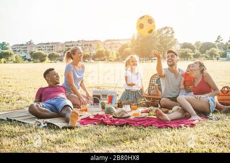 Les familles heureuses qui font un pique-nique dans le parc naturel - les jeunes parents s'amusent avec leurs enfants en été en mangeant, en buvant et en riant ensemble - l'amour Banque D'Images