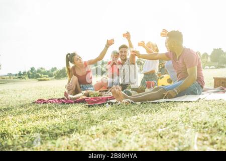 Les familles heureuses qui font un pique-nique dans le parc naturel - les jeunes parents s'amusent avec leurs enfants en été en mangeant, en buvant et en riant ensemble - l'amour Banque D'Images