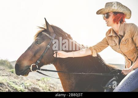 Jeune agriculteur qui monte son cheval - Cowgirl qui part pour une promenade dans une journée ensoleillée au coucher du soleil - concept de l'amour entre les gens et les animaux - Focus sur rif Banque D'Images