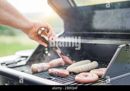 La cuisson de la viande avec de l'homme différents professionnels du barbecue dans la cour en plein air - Concept de bbq party avec les familles et amis - se concentrer sur la main - War Banque D'Images