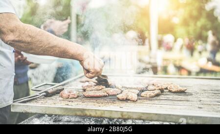 L'homme fait cuire de la viande au barbecue au dîner - le chef fait griller de la viande dans le parc en plein air - concept de manger barbecue en plein air pendant l'été - filtre chaud avec su dos Banque D'Images