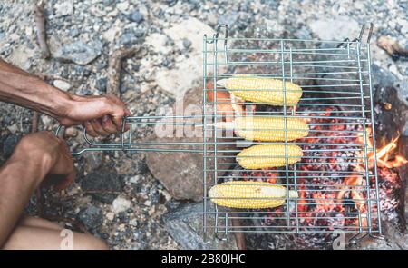 Vue de dessus du randonneur man cooking corns en camping en plein air - préparer le dîner vegan grimpeur sur bonfire - voyages, nature, la vie et l'alimentation - concept de vacances Banque D'Images