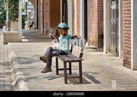 Statue d'un garçon lisant un livre assis sur un banc extérieur Banque D'Images