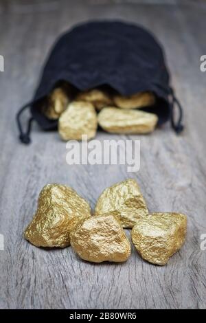 Les pépites d'or dispersent des pierres dans un sac sur une texture en bois. Banque D'Images