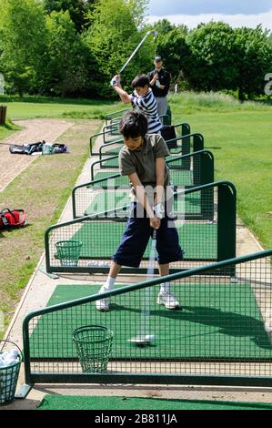 Trois joueurs de golf en action sur le terrain d'exercice. Deux jeunes garçons et un adulte qui essayent leurs compétences au Lindfield Golf Club, West Sussex, Angleterre. Banque D'Images